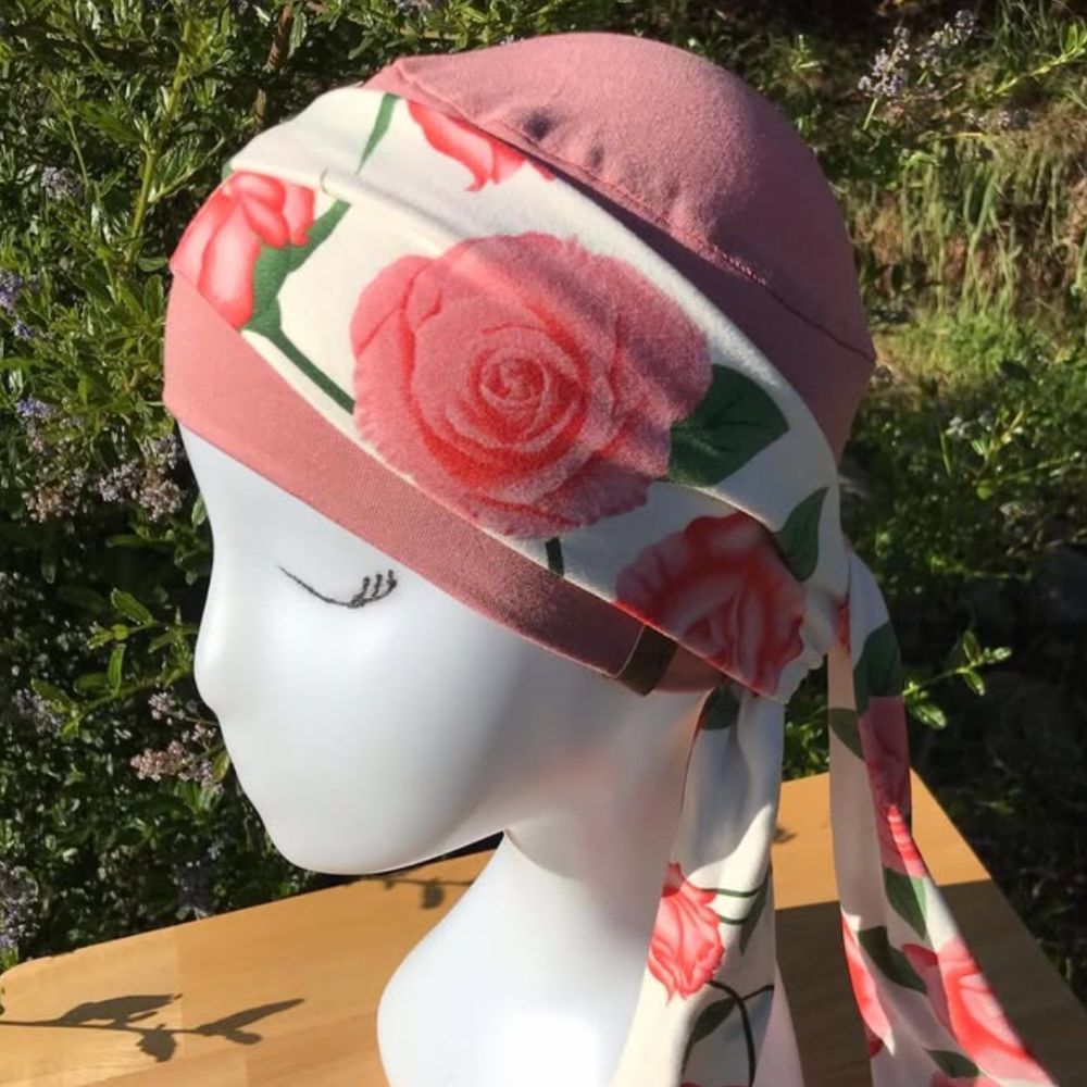 Turbante estampado con rosas y hojas, rosa y detalles morados, con tiras laterales largas.